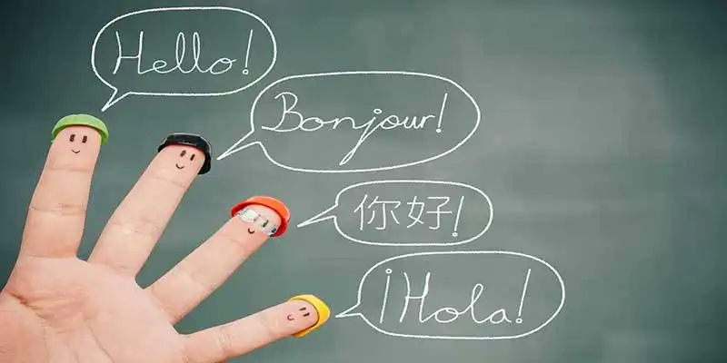 © lemontreeimages - stock.adobe.com | Four smiley fingers on a blackboard saying hello in English, French, Chinese and Spanish.